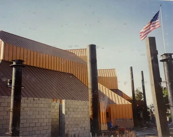 A brown metal building with a tall metal roof being constructed. 