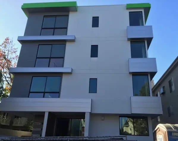 A small multi floor apartment building with metal wall paneling and a flat green metal roof.