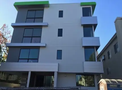 A modern white and silver multi floor apartment with a green accent roof.