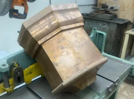 A copper downspout that is undergoing fabrication.