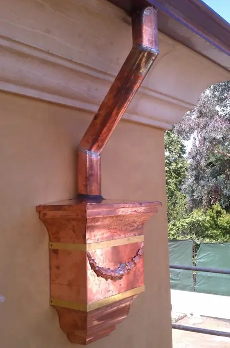 A copper rain gutter system installed on a beige house.