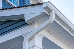 A rain gutter and downspout on the side of a white and blue house.